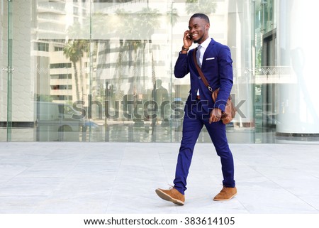 Full length portrait of a confident young businessman walking in the city talking on cell phone
