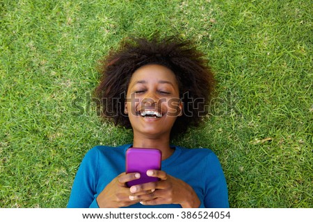 Portrait from above of a laughing woman lying on grass with cell phone
