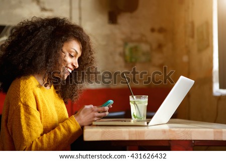 Side portrait of happy young african woman in a coffee shop using mobile phone