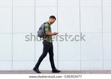 Full length side portrait of smiling man walking with backpack smart phone and headphones