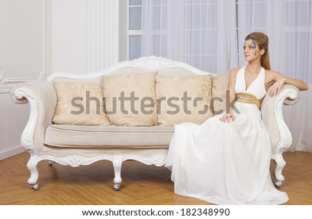 Portrait of beautiful girl with body art butterfly on her face sitting on the couch