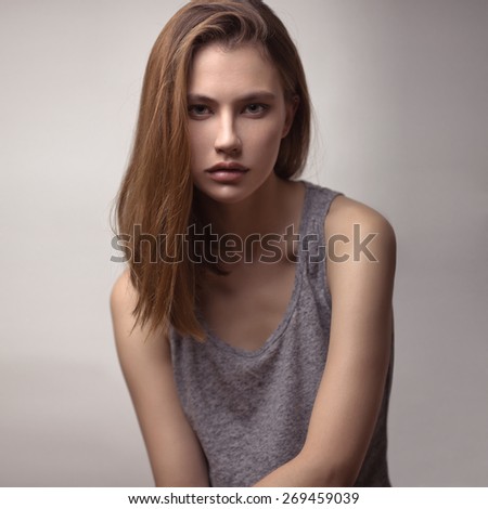 Beauty studio portrait of young stunning red-haired model in a gray tank top with long straight hair.