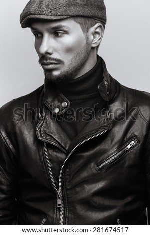 Fashion portrait of young handsome brutal bearded man in leather jacket and in cap.