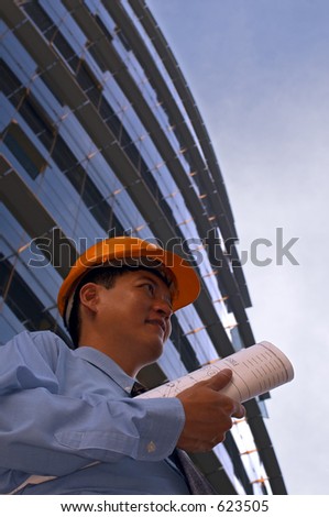 Asian male in a hard-hat holding some floor plans on his way out to a construction site