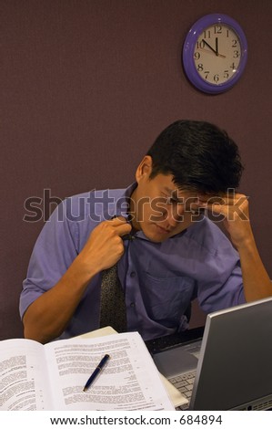 Frustrated at Work - A man working late is feeling stressed and loosens his tie. It is close to midnight and he is still working at his computer in his cubicle.