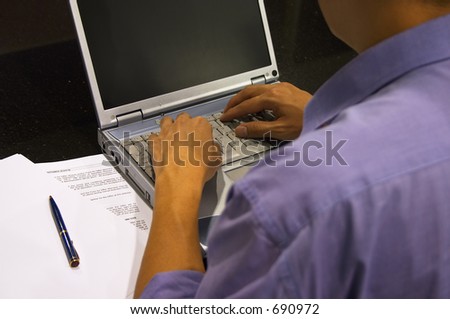 Hard at Work - A man is at his office desk typing on his laptop. Shallow depth-of-field: His back is blur. Focused on the hands and keyboard.