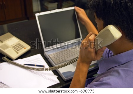 Work Discussion 2 - A man refers to his laptop while discussing work over the telephone. Graphics can be inserted later onto the blank screen.