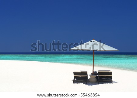 Beach chairs under an umbrella on a quiet stretch of pristine beach