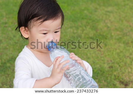 Little asian girl  drinking water from plastic bottle, after tired from a romp in the park, outdoor shot