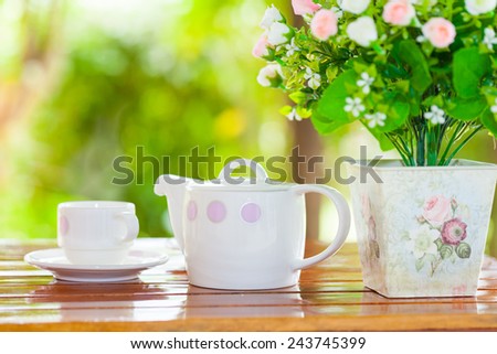 White porcelain set for tea or coffee on wooden table in the garden over blur green nature background, shallow DOF teapot in focus
