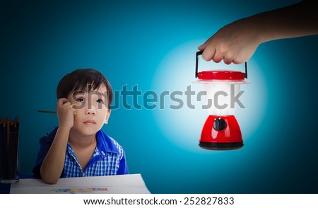 Asian (thai) boy thinking and looking up emotion at the table with images paper. Hand woman holding plastic electric lantern with lit flame on blue background, concepts of searching and direction