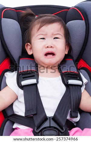 Image of little asian (thai) girl crying and fastened with security belt in safety car-seat. Concept about the safety of traveling by car, children and baby