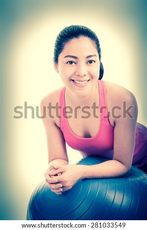 Healthy woman - beautiful asian (thai) girl smiling and leaning on fitness ball in fitness studio, vintage and retro picture style