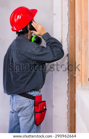 Engineer man wearing red hard hat and green earmuffs while having a phone call at construction site works