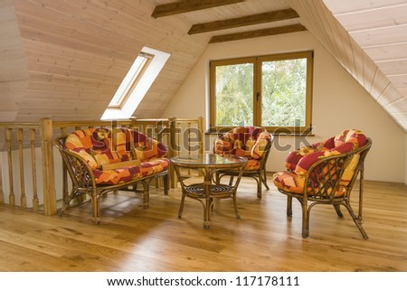 Attic room with garden furniture. Walls covered with timber planks, beams in the ceiling.