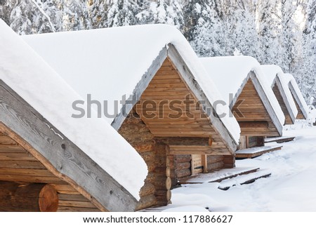 Snowy lodge roofs covered with snow at bright snowy day. Forest in background.