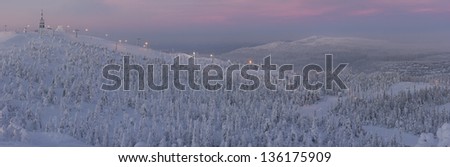 Panorama of snowy forest in mountains and ski resort at sunset in winter in Lapland, Finland