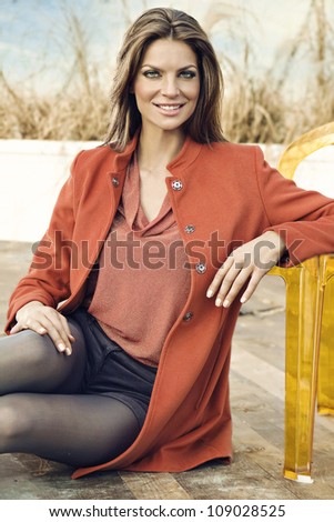 smiling confident young woman in orange coat, sitting on the porch.