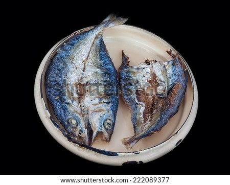 Fried salted fish in metal lid of food carrier isolated on black background