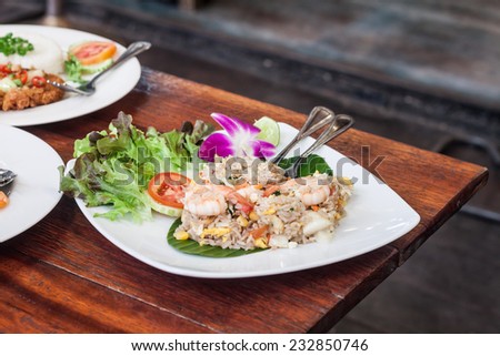 Fried rice with salted egg and shrimp on banana leaf decor by vegetable and orchid on table in restaurant