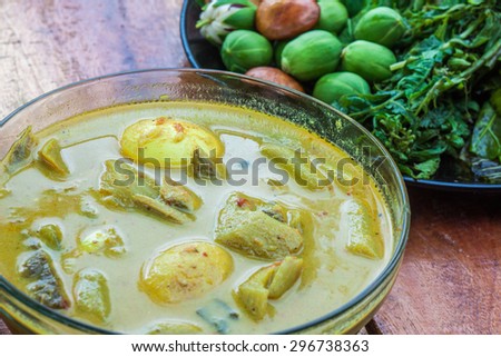 Curry egg with coconut milk and fresh vegetable in plate on wooden table