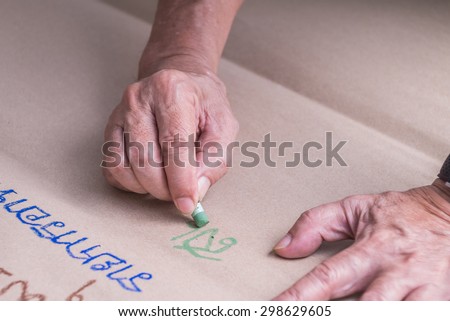 Old man\'s hand use oil pastel writing thai word on brown paper