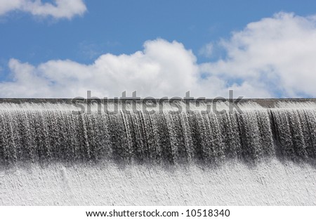 Water spilling over concrete dam wall with sky behind