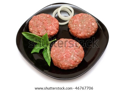 Raw hamburger patties on a black plate with onion rings and Basil garnish, isolated on white with clipping path