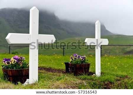 Graves with simple white crosses in front of misty mountains