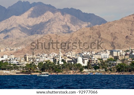 Seaside view of the jordan city of Aqaba at the Red Sea. Deep blue sea, white buildings, green trees and majestic hills.