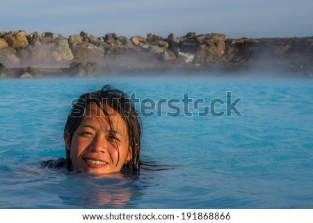 An asian girl enjoys relaxing in a hot natural pool with fantastic blue-shining water in Iceland .