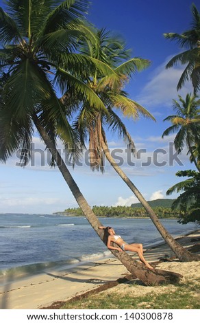 Young woman in bikini laying on leaning palm tree, Las Galeras beach, Samana peninsula, Dominican Republic
