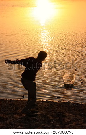 Silhouette of a boy throwing stones in a water, Khichan village, Rajasthan, India