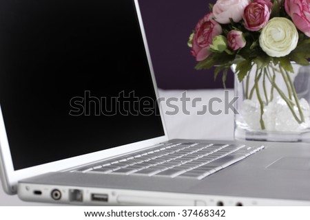 Silver laptop on a desk with a vase with pretty pink and white flowers next to it.
