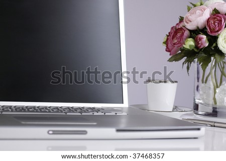 Silver laptop on a desk with a vase with pretty pink and white flowers next to it.