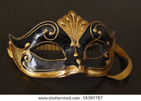Beautiful Venetian mask in black and gold on top of an old leather table.