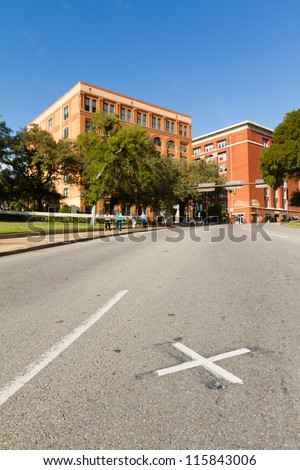 X on the road where President John F. Kennedy was assassinated with the Book Depository in the background