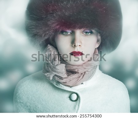 Fashion girl model posing in coat and white furry hat. Winter Beautiful Woman in Luxury clothes over bokeh Christmas Lights background.