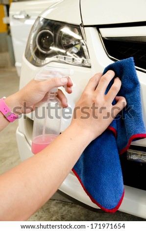 hand with microfiber cloth wiping a car with spray wax in car-wash shop
