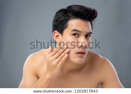 Portrait of shirtless young handsome Asian man checking his face for skin care and beauty concepts, studio shot isolated on gray background