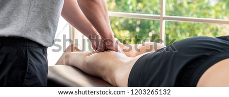 Male therapist giving leg massage to athlete patient on the bed in clinic for sports physical therapy concept, banner proportion