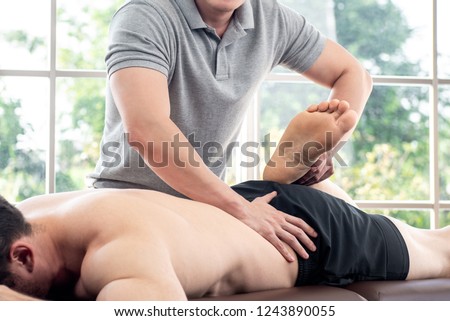 Physical therapist giving massage and stretching to athlete male patient on the bed in clinic, sports medicine concept