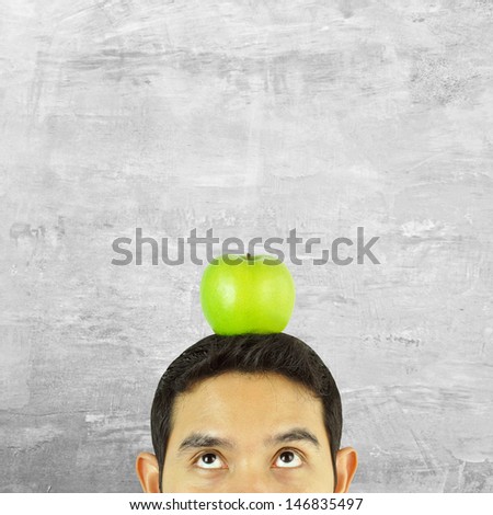 Thoughtful man with green apple over his head on old concrete wall background