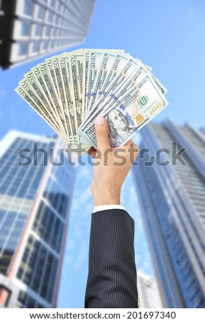 Hand holding money - United States Dollars (or USD) - on building background