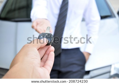 Hand giving a car key to another man - car sale & rental service concept