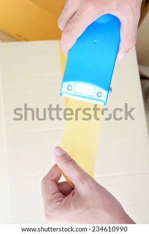 Hands holding masking tape dispenser, taping a box