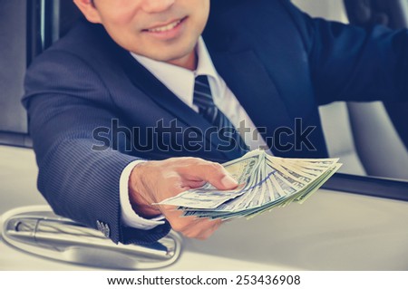 Business man giving money (US dollar bills) while sitting in a car; car insurance, sale & rental concepts - vintage (retro) style color effect