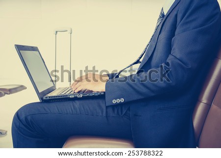 Businessman using laptop or notebook computer while sitting on the chair at the airport - vintage (retro) style color effect with soft focus