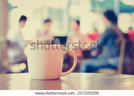 Coffee cup on the table with people in coffee shop as blur background - vintage (retro) style color effect