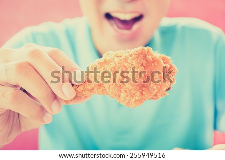 A man with opening mouth about to eat deep fried chicken leg or drumstick - vintage style color effect